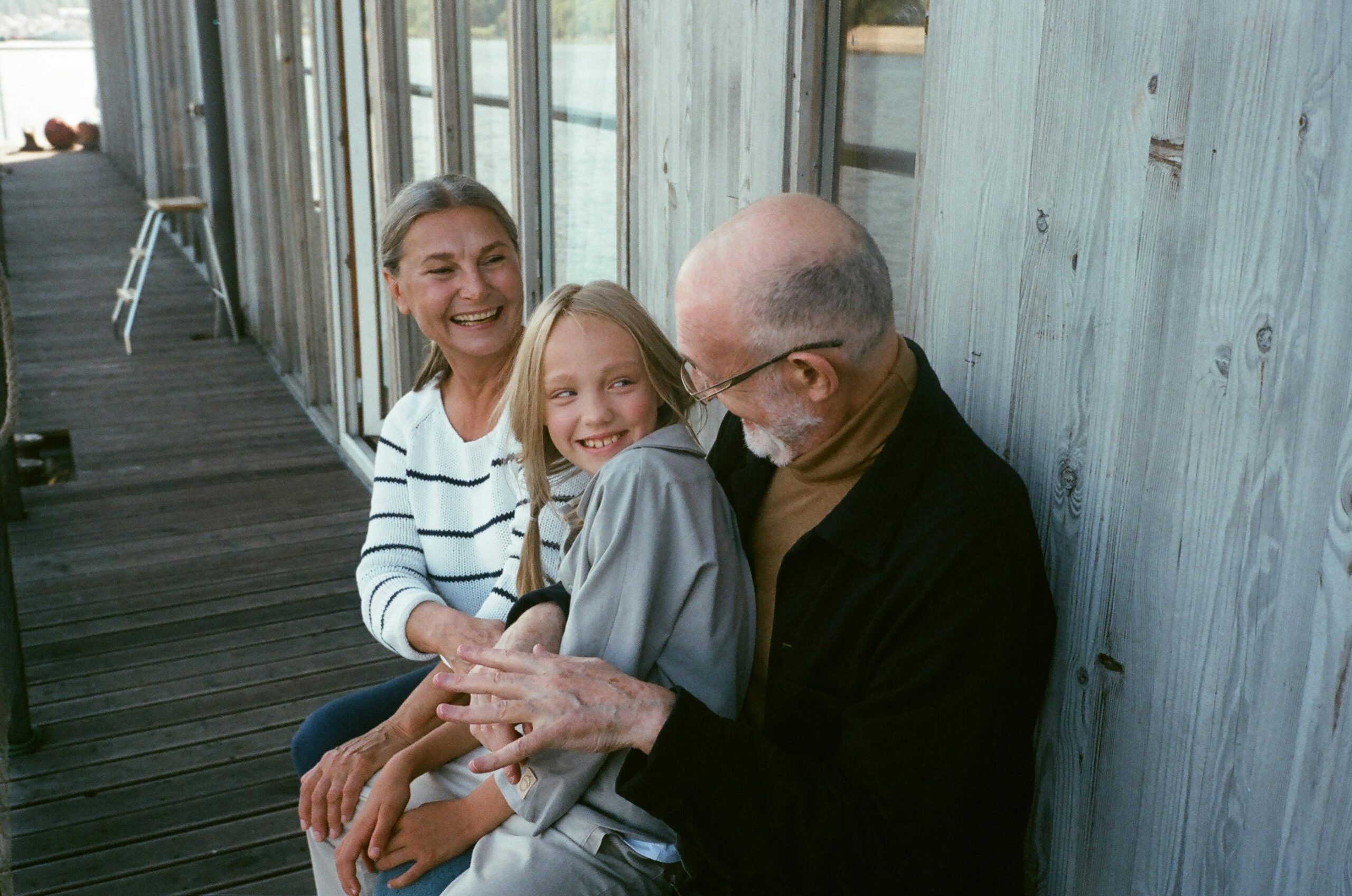 Three generations of a family smiling and connecting on a wooden porch near water