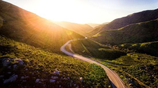 Sunset over winding road through green hills symbolizing a journey toward summer mental wellness and healing.