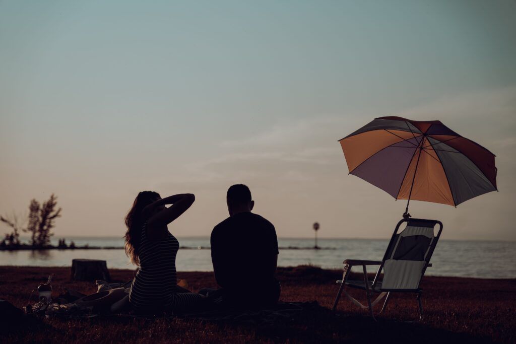 Couple sitting together by the water at sunset, reflecting and spending quality time to create lasting change in their relationship.