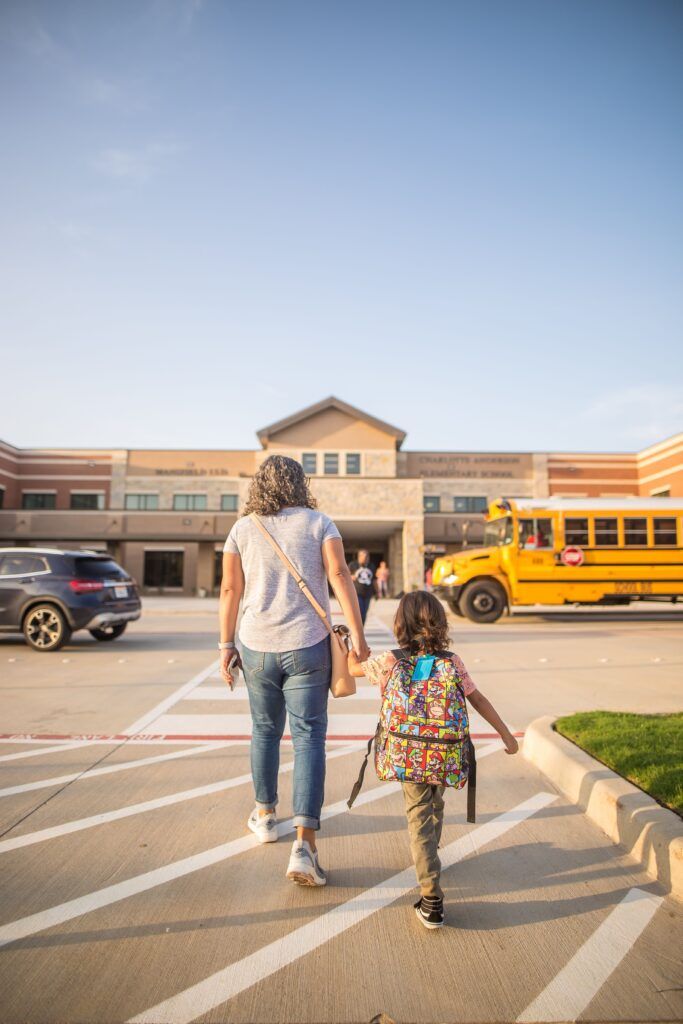 Parent walking with a child carrying a backpack into school, representing back-to-school routines that support family wellbeing, consistency, and a positive school transition.