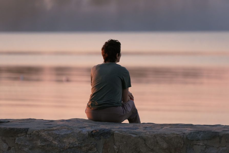 Understanding Your Patterns: The Path to Meaningful Change Person sitting by the water at sunset, reflecting quietly, representing understanding your patterns and developing greater self-awareness.